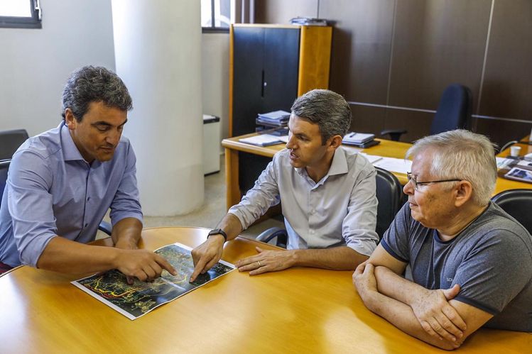 Presidente Gilson Santos sentado na mesa com Fernando Furiatti e Milton Campos apontando para um mapa da região metropolitana de Curitiba.